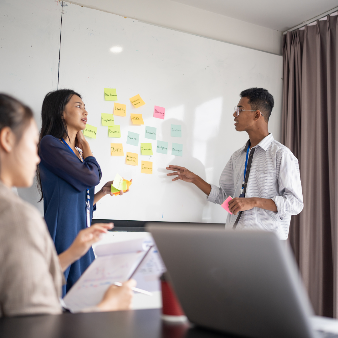 فريق عمل يناقش أفكارًا تسويقية أمام سبورة مليئة بملاحظات لاصقة ملوّنة، في ورشة عمل تعكس طريقة عمل أفضل شركات التسويق الإلكتروني لبناء حملات مبتكرة.
