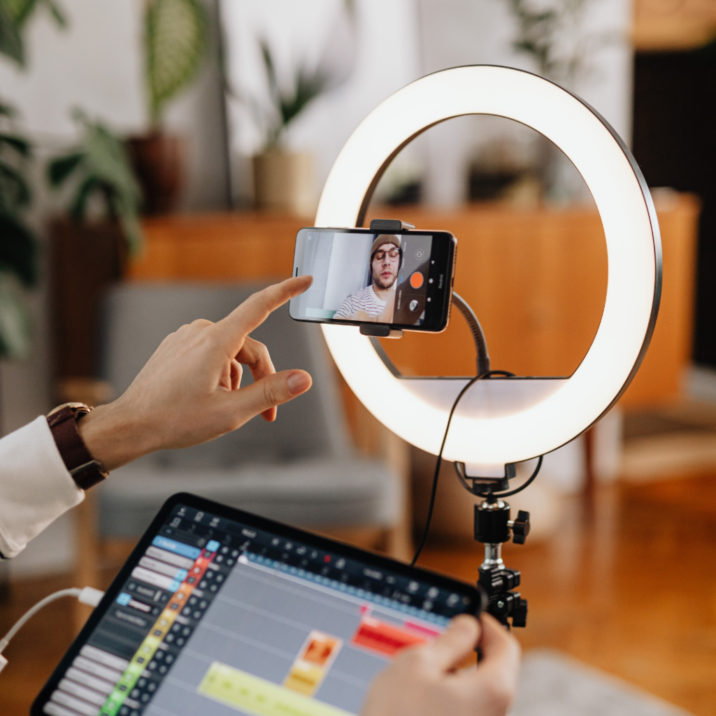 صانع محتوى يجهز هاتفه الذكي على حامل مع حلقة إضاءة (Ring Light) لتصوير فيديو احترافي لمنصة يوتيوب، مع وجود جهاز لوحي أمامه لعملية المونتاج.